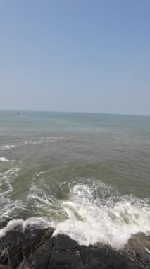 Okyanus dalgaları kıyıdaki büyük siyah kayalara çarpıyor.