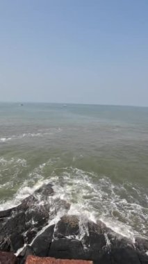 Okyanus dalgaları kıyıdaki büyük siyah kayalara çarpıyor.