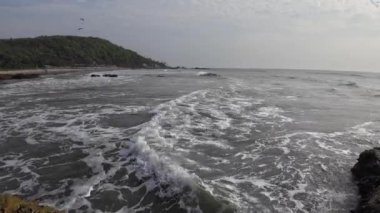 Okyanus dalgaları kıyıdaki büyük siyah kayalara çarpıyor.