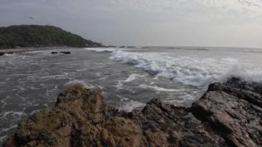 Okyanus dalgaları kıyıdaki büyük siyah kayalara çarpıyor.