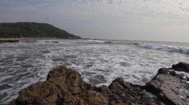 Okyanus dalgaları kıyıdaki büyük siyah kayalara çarpıyor.