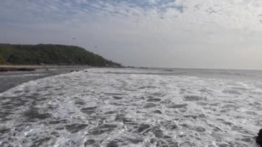 Okyanus dalgaları kıyıdaki büyük siyah kayalara çarpıyor.