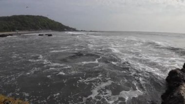 Okyanus dalgaları kıyıdaki büyük siyah kayalara çarpıyor.