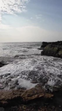 Okyanus dalgaları kıyıdaki büyük siyah kayalara çarpıyor.