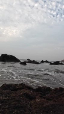 Okyanus dalgaları kumsaldaki küçük siyah kayaların arasına çarpıyor.