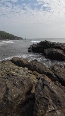 Okyanus dalgaları kıyıdaki büyük siyah kayalara çarpıyor.