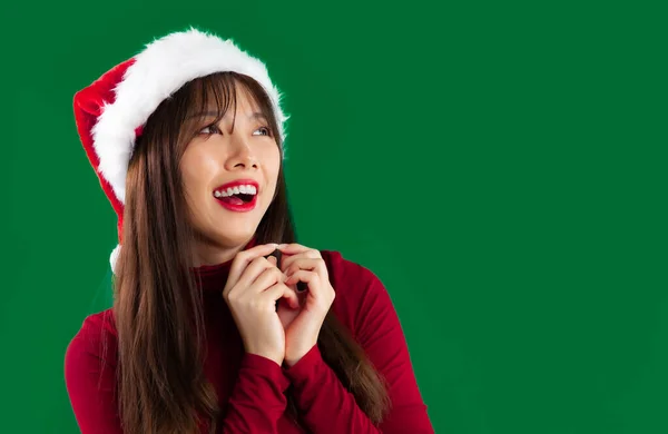 Happy Asian woman long hairstyle in red long sleeve t-shirt wear santa hat posing green background.