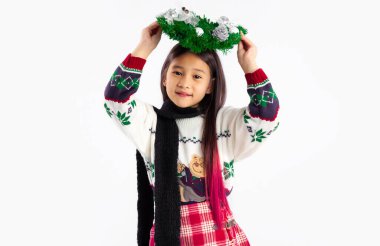 Asyalı öğrenci kafasında Noel çelengi ile beyaz arka planda poz veriyor..