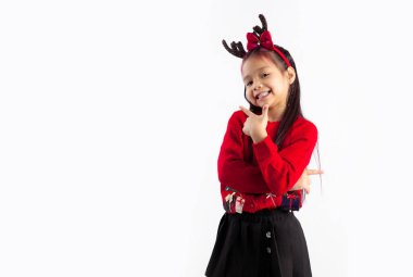 Kırmızı kazaklı küçük Asyalı çocuk Noel temalı kostüm giymiş gülümsüyor ve beyaz arka planı işaret ediyor..