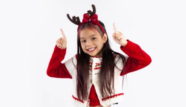 Kırmızı beyaz tişörtlü Asyalı çocuk Noel temalı kostüm giymiş kameraya gülümsüyor ve parmakları beyaz arka planı işaret ediyor. Mutlu Noeller..