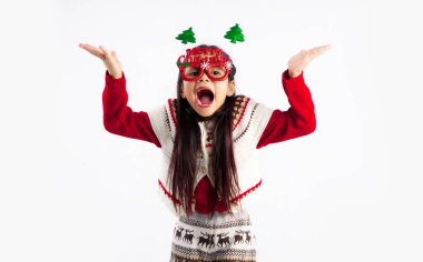 Kırmızı kazaklı küçük Asyalı çocuk Noel temalı kostüm giymiş ağzı açık poz veriyor ve beyaz arka planı işaret ediyor..