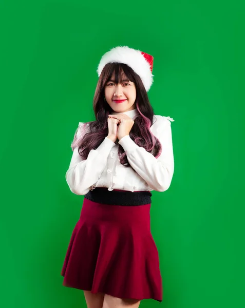 Asian woman long hairstyle wearing santa hat white and red cloth posing on green screen background. Merry Christmas concept.