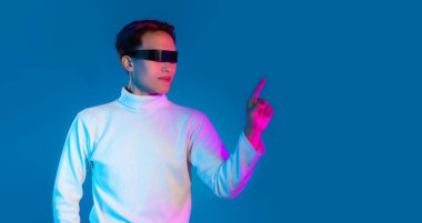 Asyalı adam çalarken VR gözlük takıyor ve mavi arka plana dokunuyor. Metaverse konsepti