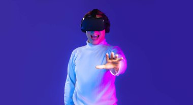 VR gözlük takan Asyalı adam koyu mavi arka planda dokunuşunu izliyor. Metaverse konsepti