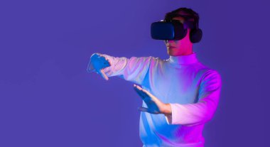 Uzun kollu beyaz tişörtlü Asyalı adam video gözlüklü kulaklık takıyor ve internette mor arka planda oyun oynuyor. Metaverse eşleşmesi