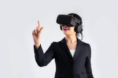 Young asian businesswoman in black suit wearing vr goggles headset finger pointing and touching on white background. Metaverse concept.	