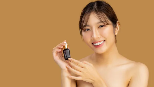 Beauty and skin care. young asian woman portrait face with skin care healthy holding bottle of serum looking cemera on beige color background.