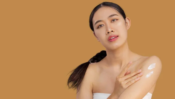 Beauty asian woman portrait with skin care healthy and skin applying cream on clean upper arm. beige color background
