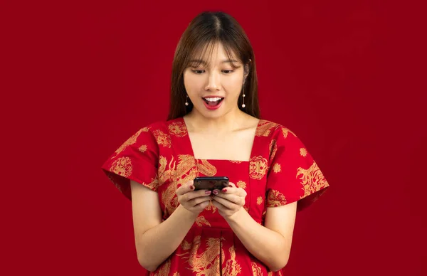Young asian woman long hairstyle in red dress using smartphone to shopping online, chating and text message on red background.