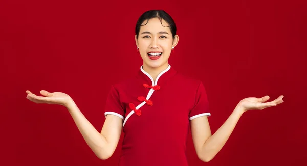 Beautiful asian woman wearing traditional chinese dress posing smiling looking camera and hand pointing for choosing red background