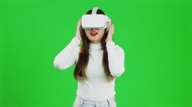 Virtual Reality concept. Front view of a young asian woman looking around, wearing a white shirt and a VR headset, greenscreen