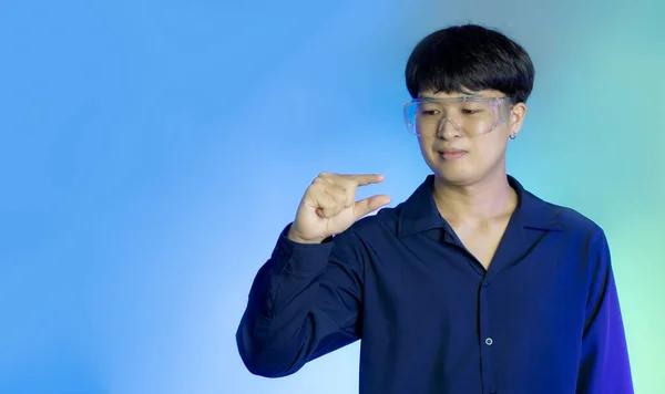 Asian man wearing vr glasses finger pinching virtual reality world screen on blue background. Technology and AR glasses.