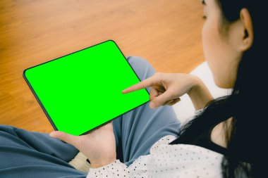 Evinde ya da ofisinde boş yeşil ekranlı siyah dijital tablet taşıyan Asyalı genç bir kadının görüntüsü..