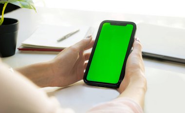 Close-up Woman sitting and holding blank screen mock up mobile phone on blur tabe background.	