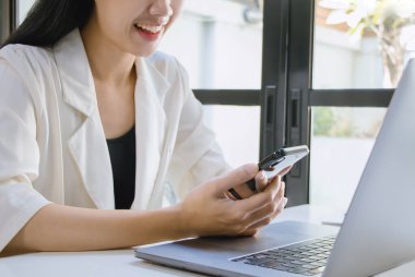 Ofiste boş zamanlarında akıllı telefon kullanan Asyalı bir kadın. Telefonu kullanma konsepti günlük hayatta gereklidir..