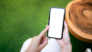 Close-up of woman hand holding a smartphone white screen is blank the background is blurred. obile phone Mockup.	