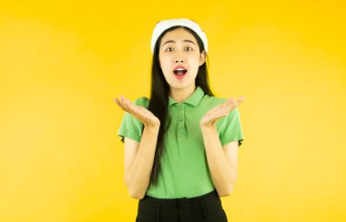 Asyalı kadının Noel Baba şapkası giymesine şaşırdım. Sarı arka planda izole edilmiş kırmızı Noel Baba şapkası.