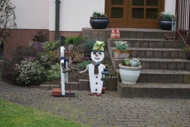 Bahçede dekorasyon. Bir kadın ve bir erkek evin girişindeki kardan adamlardır. Bahçenin süsü olarak. Berlin, Almanya