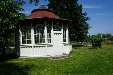 Haziranda etrafı bitki örtüsüyle çevrili bir parkta, nehrin kıyısındaki ahşap çardak. Berlin yakınlarındaki Ruedersdorf, Almanya 