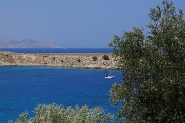 Bir yelkenli Lindos açıklarında Akdeniz 'de yelken açıyor. Lindos, Yunanistan 'ın Dodecanese kentindeki Rodos adasında bir arkeolojik alan, bir balıkçı köyü ve eski bir belediyedir..