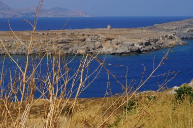 Ağustosta eski yel değirmeninin karşısındaki Lindos sahilinde kurak bitki örtüsü var. Lindos, Yunanistan 'ın Dodecanese kentindeki Rodos adasında bir arkeolojik alan, bir balıkçı köyü ve eski bir belediyedir.. 