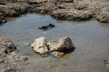 Pefki 'deki Akdeniz kıyısında sular çekildikten sonra plajda lastik parmak arası terlikler deniz suyunda yüzer. Pefkos ya da Pefki, Rhodes Adası 'nın doğu kıyısında bulunan ünlü bir sahil beldesidir. Pefkos veya Pefki, Rodos Adası, Yunanistan 