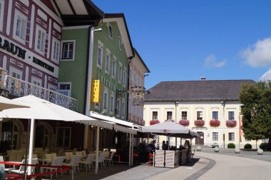 Mondsee, Salzkammergut, Avusturya - 12 Eylül 2022: Mondsee 'ye gelen ziyaretçiler, neoklasik binalardaki parlak yüzlü kafelerin bazılarının açık hava oturma alanlarının keyfini çıkarıyorlar.