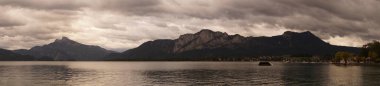 Fotoğraf panoraması. Mondsee 'den bulutlu bir eylül akşamında Mondsee' ye yelkenli tekneleri ve Alpler dağlarıyla manzaralı bir göl manzarası. Mondsee, Salzkammergut 'un Yukarı Avusturya bölgesinde bulunan bir göldür. Avusturya 