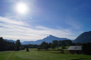 Sonbahar güneşi, Mondsee Gölü yakınlarındaki Ferrata yoluyla Drachenwand civarındaki dağlık bir alp manzarasının üzerinde bulutlu bir gökyüzünde parlar. St. Lorenz, Yukarı Avusturya, Avusturya