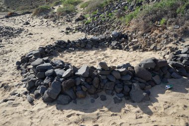 Atlantik Okyanusu sahillerinde istiflenmiş taşlar tatilcileri rüzgardan korur. Esquinzo, Fuerteventura, Las Palmas, Kanarya Adaları, İspanya. 