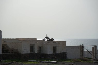 Costa Calma, Fuerteventura, İspanya - 22 Ekim 2022: Matas Körfezi 'ndeki Rancho de Matas Blancas binasının çatısında eski paslı bir motosiklet duruyor.. 