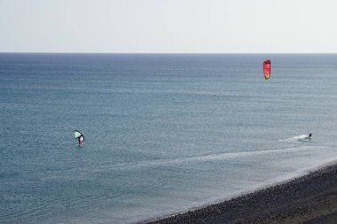 A kiteboarder and a wingfoiler ride their boards on the waves of the Atlantic Ocean in Matas Bay. Kiteboarding or kitesurfing is a sport that involves using wind power. Costa Calma, Fuerteventura, Las Palmas, Spain.  clipart