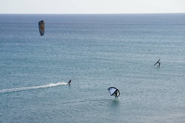 A kiteboarder and wingfoilers ride their boards on the waves of the Atlantic Ocean in Matas Bay. Kiteboarding or kitesurfing is a sport that involves using wind power. Costa Calma, Fuerteventura, Las Palmas, Spain. clipart