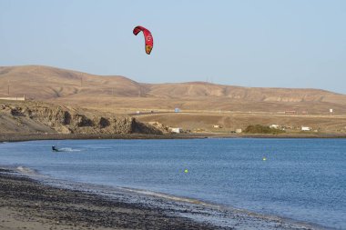 Bir uçurtma sörfçüsü, Matas Bay 'de, Matas de Blancas plajı boyunca sonbaharda Atlantik Okyanusu' nun dalgaları üzerinde sörf tahtasına biner. Uçurtma sörfü ya da uçurtma uçurmak rüzgar enerjisi gerektiren bir spordur. Costa Calma, Fuerteventura, Kanarya Adaları.