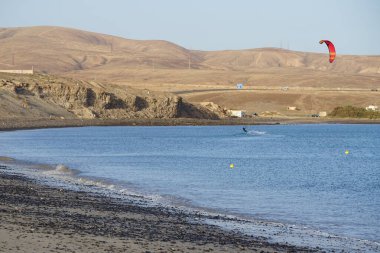 Bir uçurtma sörfçüsü, Matas Bay 'de, Matas de Blancas plajı boyunca sonbaharda Atlantik Okyanusu' nun dalgaları üzerinde sörf tahtasına biner. Uçurtma sörfü ya da uçurtma uçurmak rüzgar enerjisi gerektiren bir spordur. Costa Calma, Fuerteventura, Kanarya Adaları.