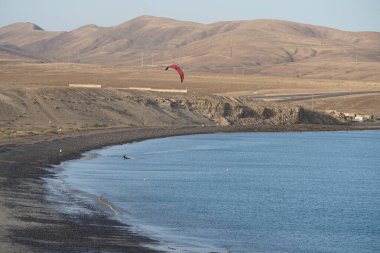 Bir uçurtma sörfçüsü, Matas Bay 'de, Matas de Blancas plajı boyunca sonbaharda Atlantik Okyanusu' nun dalgaları üzerinde sörf tahtasına biner. Uçurtma sörfü ya da uçurtma uçurmak rüzgar enerjisi gerektiren bir spordur. Costa Calma, Fuerteventura, Kanarya Adaları.