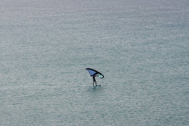 Bir kanat folyosu, Matas Körfezi 'ndeki Atlantik Okyanusu' nun dalgaları boyunca folyoyla yol alır. Kanat kanat çırpma, kanat çırpma veya kanat çırpma rüzgarı yakalamak için bir el kanadı kullanmayı ve suyun yüzeyinde bir levhayı itmeyi içerir. Costa Calma, İspanya.  