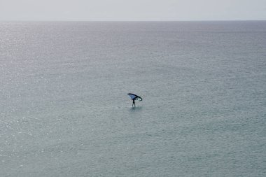 Bir kanat folyosu, Matas Körfezi 'ndeki Atlantik Okyanusu' nun dalgaları boyunca folyoyla yol alır. Kanat kanat çırpma, kanat çırpma veya kanat çırpma rüzgarı yakalamak için bir el kanadı kullanmayı ve suyun yüzeyinde bir levhayı itmeyi içerir. Costa Calma, İspanya.  