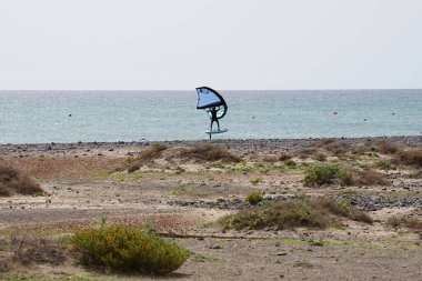 A wingfoiler rides a foilboard across the waves of the Atlantic Ocean in Matas Bay. Wing foiling, wing surfing or winging involves using a handheld wing to catch the wind and propel a foilboard across the surface of the water. Costa Calma, Spain.   clipart