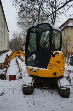 Berlin, Almanya - 3 Aralık 2022: Aralık 'ta bir apartmanın önünde kar kaplı bir hendeğin yanında bir JCB 8025 kazıcısı duruyor.